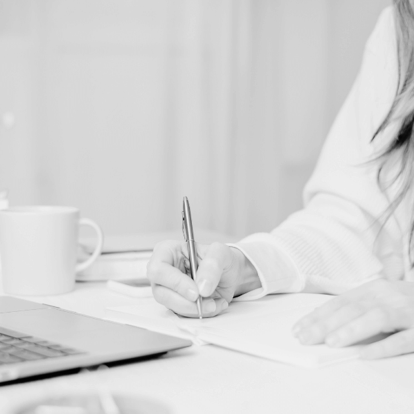 woman's arm writing notes at a desk with a laptop on it